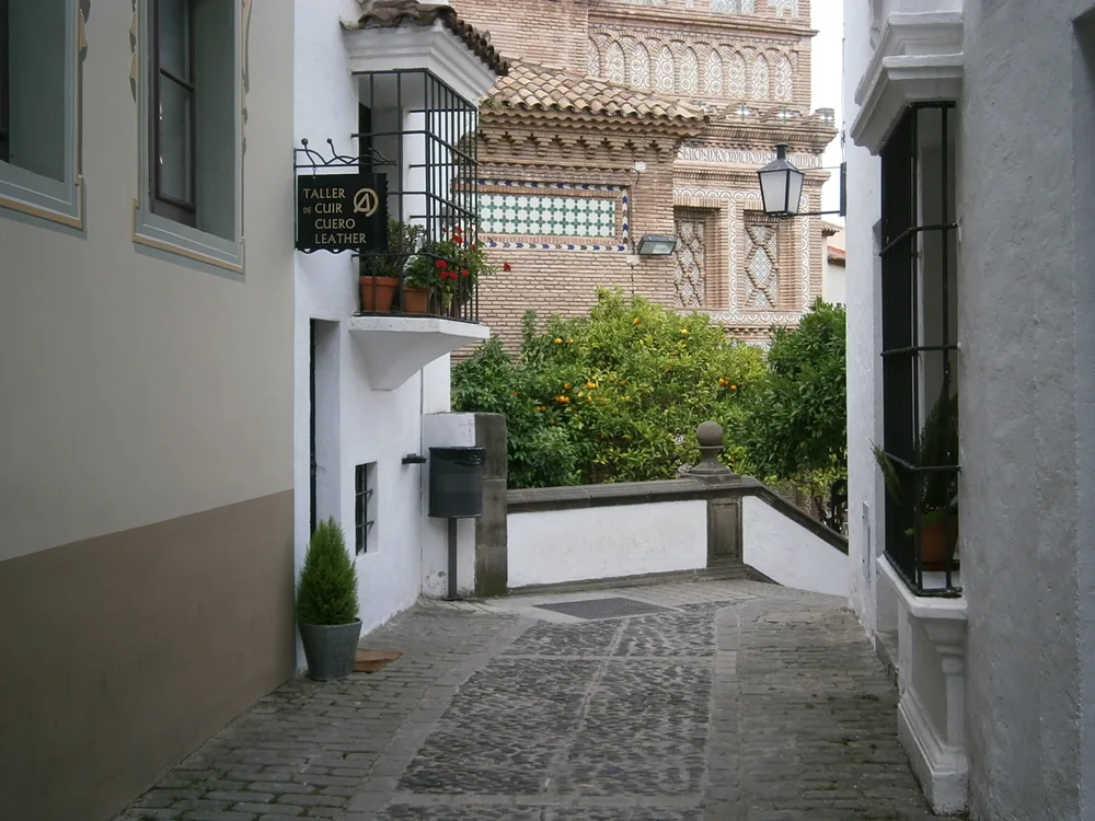 A cobbled lane between whitewashed buildings in Poble Espanyol, with orange trees behind a low wall